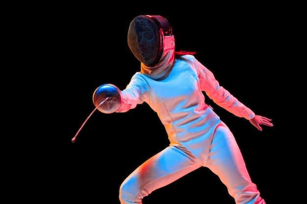 Teen girl in fencing costume with sword in hand isolated on black background, neon light.