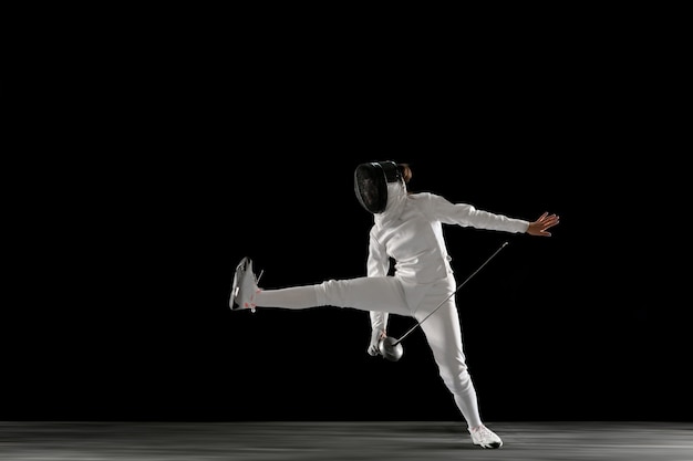 Free photo teen girl in fencing costume with sword in hand isolated on black