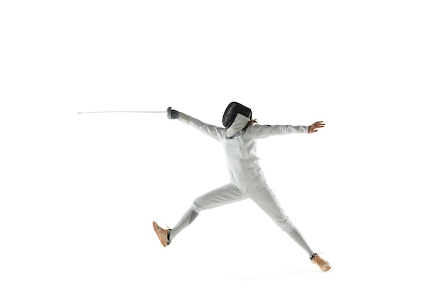 Teen girl in fencing costume with sword in hand isolated on white studio background. Young female caucasian model practicing and training in motion, action. Copyspace.