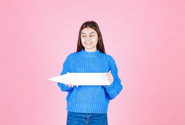 teen girl holding an arrow out of paper as a pointer aside.