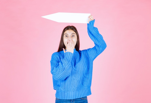 Free photo teen girl holding an arrow out of paper as a pointer aside.