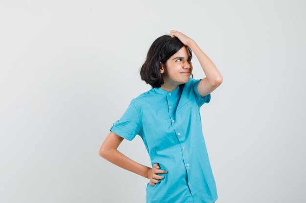 Teen girl holding hand on her head in blue shirt and looking confused.