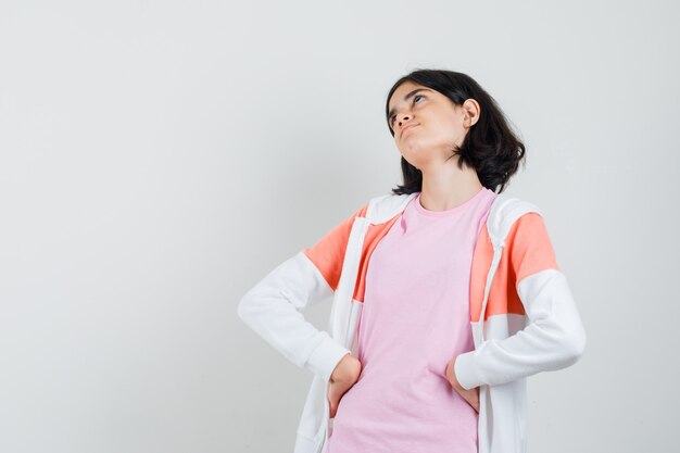 Teen girl holding hands on her waist while looking up in jacket,pink shirt and looking hesitant