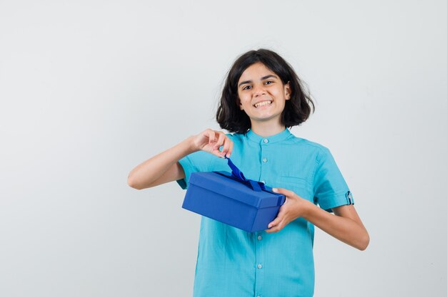 Teen girl holding present box while smiling in blue shirt and looking happy.