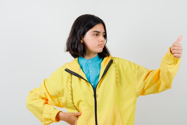 Бесплатное фото Девушка в желтой куртке показывает палец вверх и выглядит довольным, вид спереди.