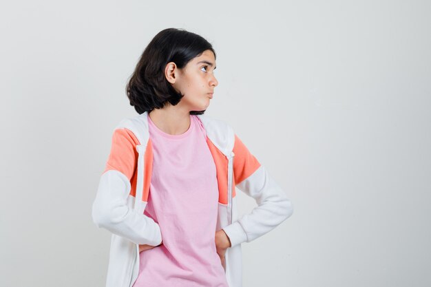 Девушка в куртке, розовой рубашке смотрит в сторону, держась за талию и смотрит сосредоточенно.