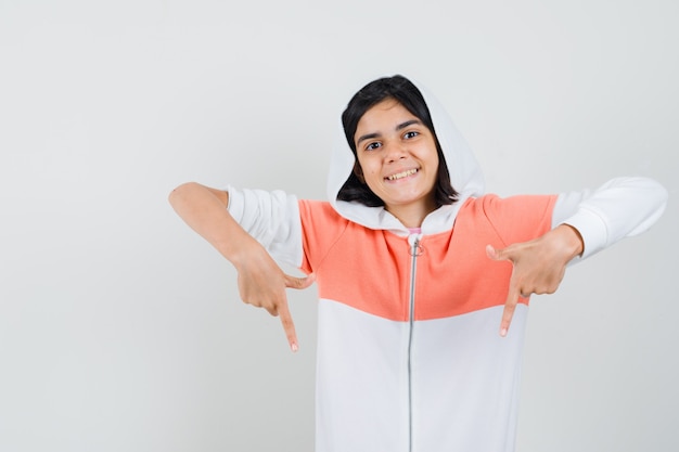 Teen girl in jacket pointing down and looking cheerful.