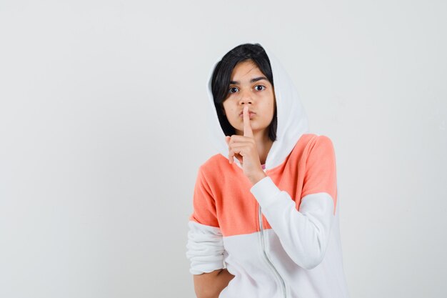 Teen girl in jacket showing silence gesture and looking silent.