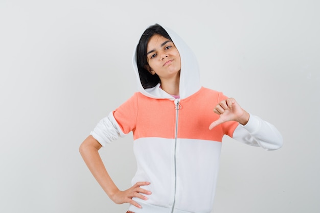 Teen girl in jacket showing thumb down and looking discontented.