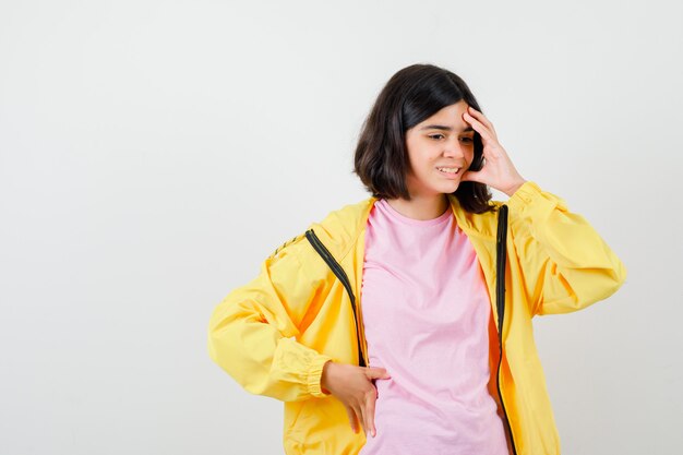 Teen girl keeping hand on head in t-shirt, jacket and looking stressed. front view.