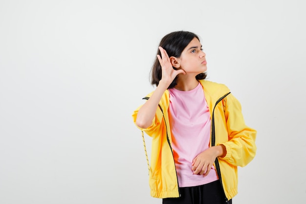 Девушка-подросток подслушивает частный разговор в футболке, куртке и выглядит сосредоточенным. передний план.