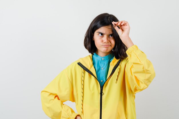 Teen girl playing with her hair in yellow jacket and looking thoughtful. front view.