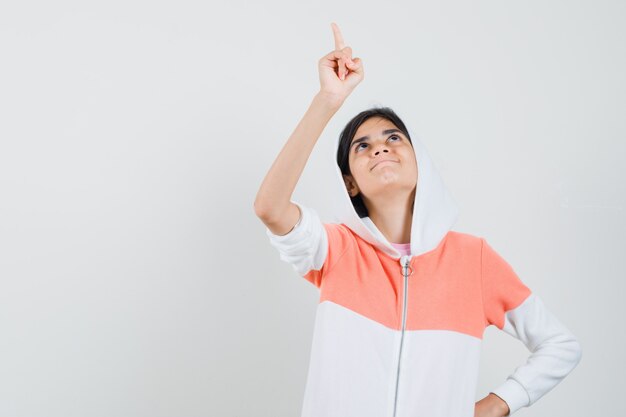 Teen girl pointing at something in white jacket and looking focused.