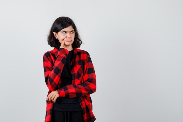 Ragazza teenager che preme il dito sulla fossetta in camicia casual e che sembra pensierosa. vista frontale.