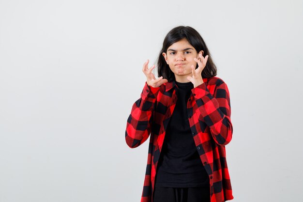 Teen girl pretending to catch something in t-shirt, checkered shirt and looking bored , front view.