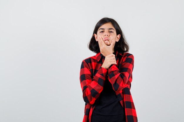 Teen girl pulling down her skin in t-shirt, checkered shirt and looking disappointed. front view.