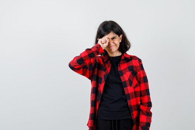 Teen girl rubbing her eye in casual shirt and looking curious , front view.