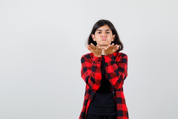 Teen girl sending air kiss in t-shirt, checkered shirt and looking pretty. front view.