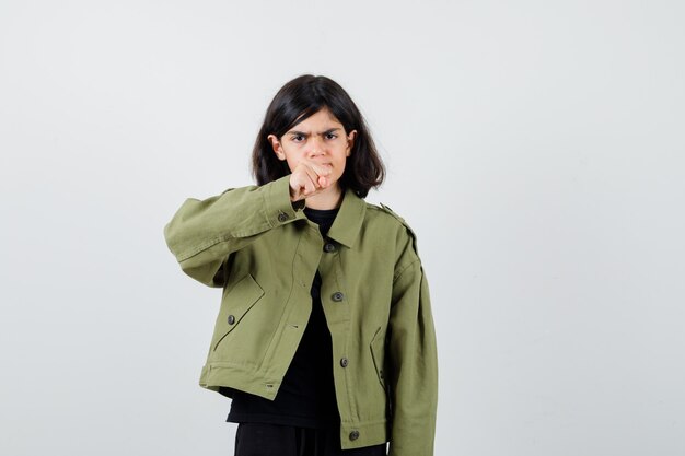 Teen girl showing clenched fist in t-shirt, jacket and looking annoyed , front view.