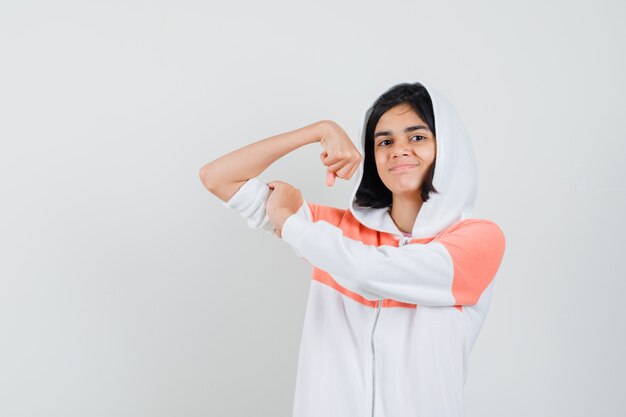 Teen girl showing her arm muscle in sweatshirt and looking satisfied.