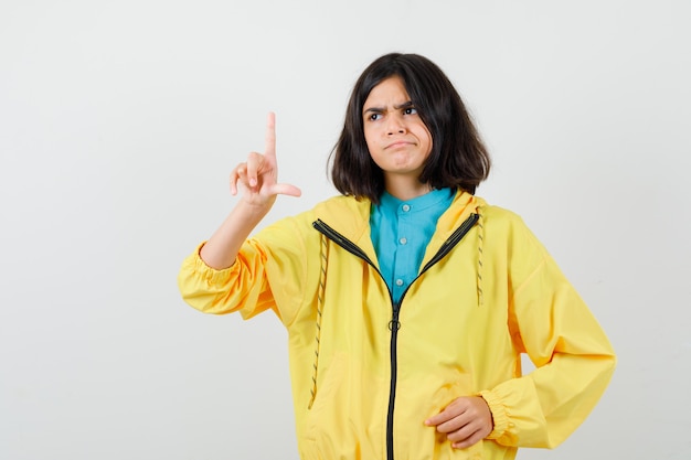 Ragazza teenager che mostra il segno del perdente in giacca gialla e sembra delusa. vista frontale.