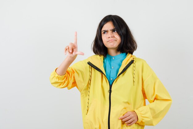 Девушка-подросток показывает знак неудачника в желтой куртке и выглядит разочарованным. передний план.