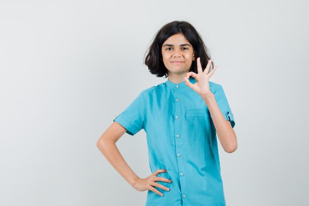 Teen girl showing ok gesture in blue shirt and looking glad.