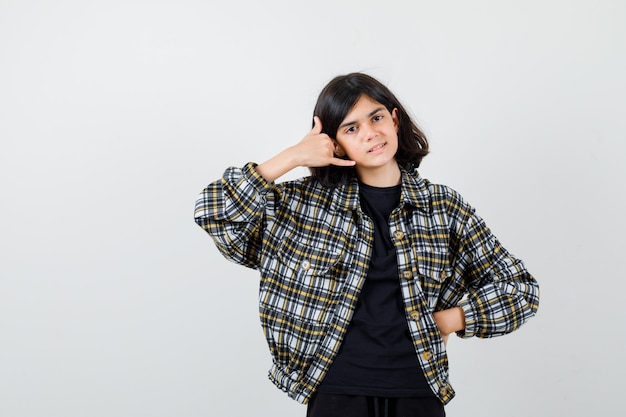 Teen girl showing phone gesture in casual shirt and looking confident , front view.