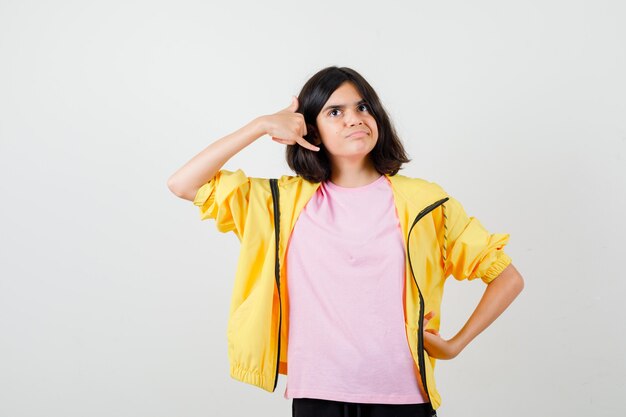 Девушка-подросток показывает жест телефона, позирует в футболке, куртке и выглядит блаженно. передний план.
