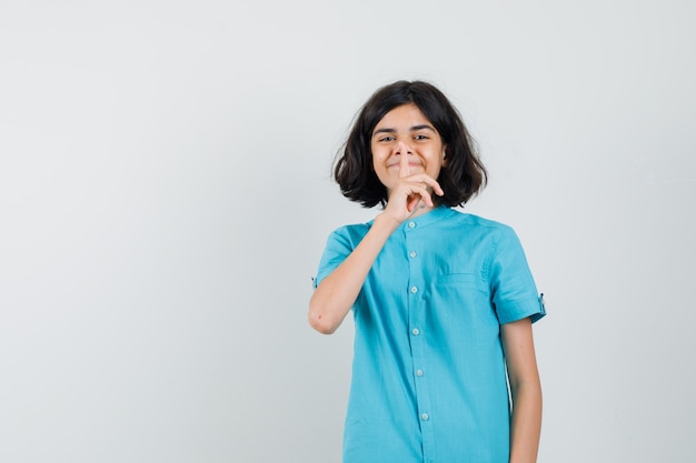 Девушка-подросток показывает жест молчания в синей рубашке