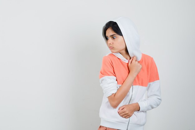 Teen girl stepping aside in white jacket and looking scared.