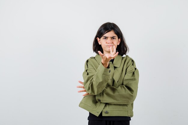 Девушка-подросток протягивает руку в вопросительном жесте в футболке, куртке и выглядит серьезным, вид спереди.