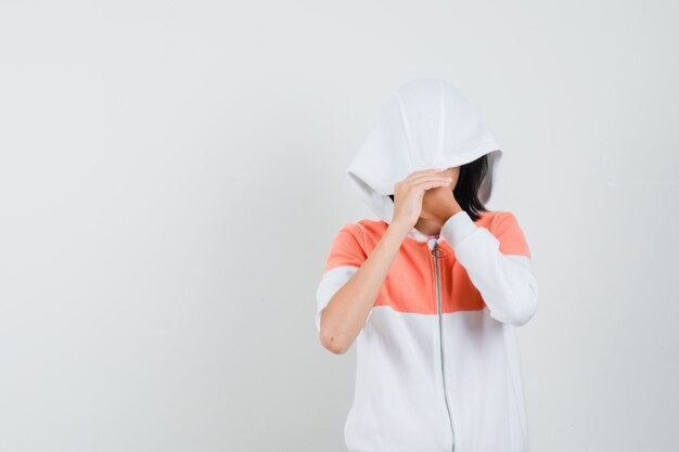 Teen girl in sweatshirt pulling cap over her face.