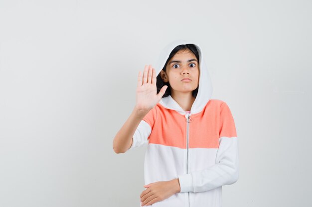 Teen girl in sweatshirt showing stop gesture and looking attentive.