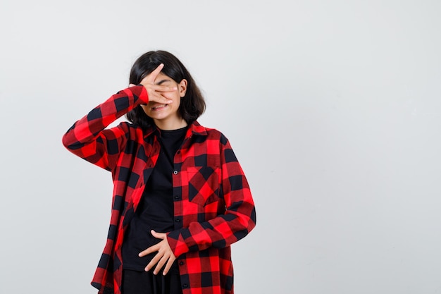 Teen girl in t-shirt, checkered shirt holding hand on face and looking sorrowful , front view.