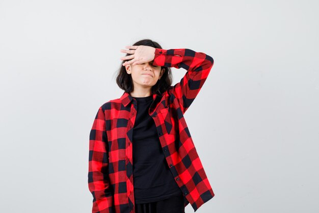 Teen girl in t-shirt, checkered shirt holding hand on forehead and looking disappointed , front view.