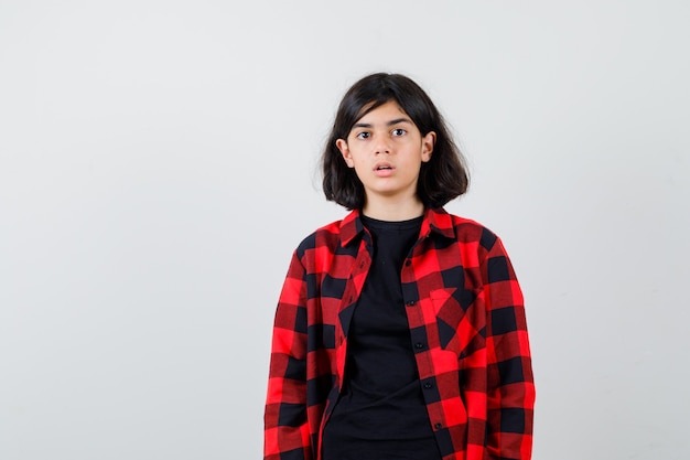 Teen girl in t-shirt, checkered shirt and looking perplexed , front view.