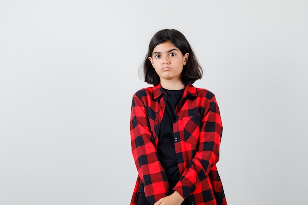 Teen girl in t-shirt, checkered shirt and looking perplexed. front view.