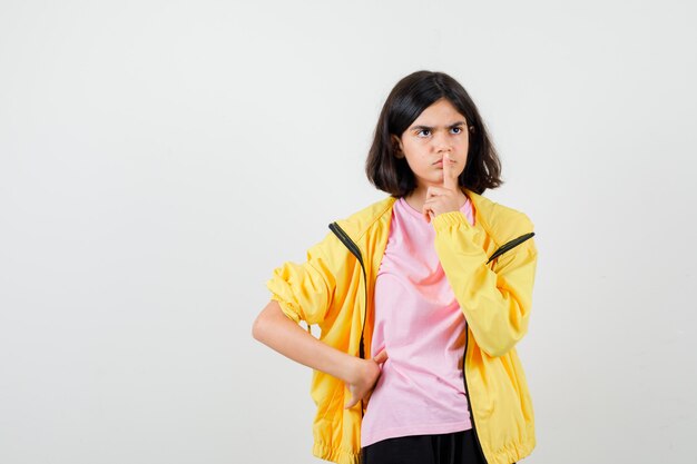 Девушка в футболке, куртка показывает жест молчания, смотрит в сторону и смотрит сосредоточенно, вид спереди.