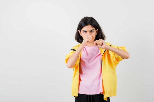 Teen girl in t-shirt, jacket standing in fight pose and looking focused , front view.