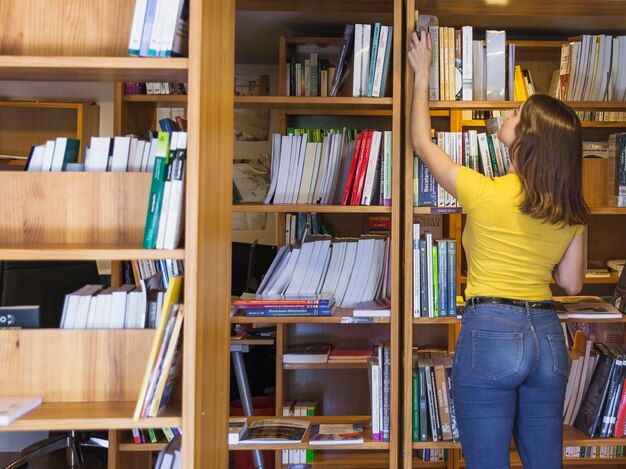 Teen girl taking book from top of bookcase