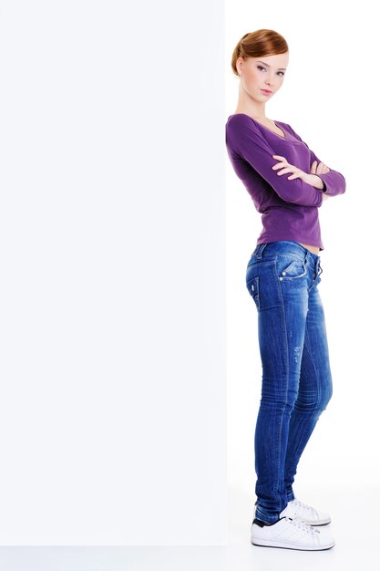 The teen girl with a serious sight at  face standing near the blank publicity board