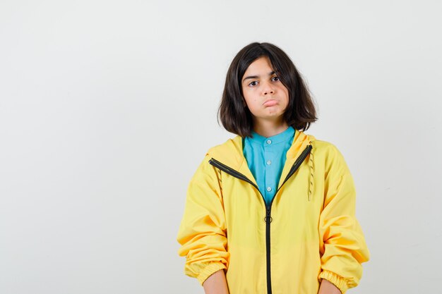Девушка в желтой куртке, изгибая нижнюю губу и выглядящая невежественной, вид спереди.