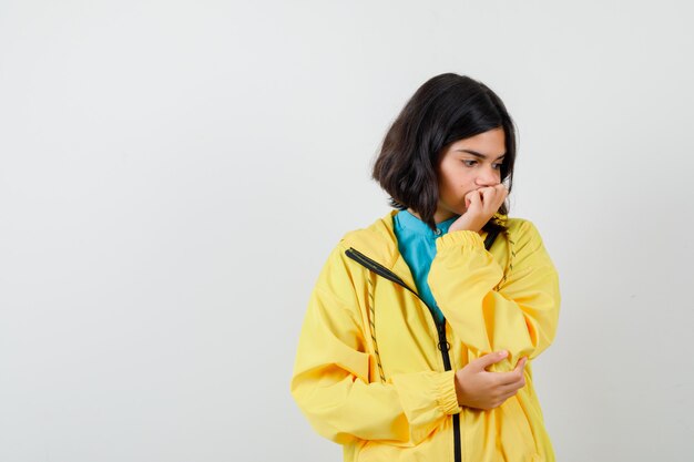 Teen girl in yellow jacket thinking about something, looking down and looking dismal , front view.