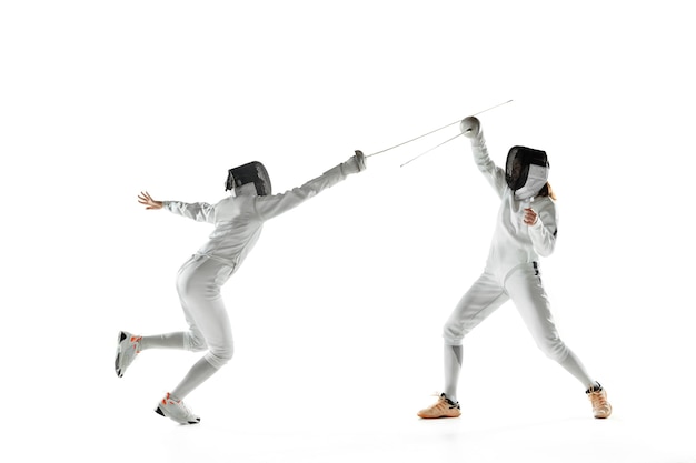 Teen girls in fencing costumes with swords in hands isolated on white studio wall
