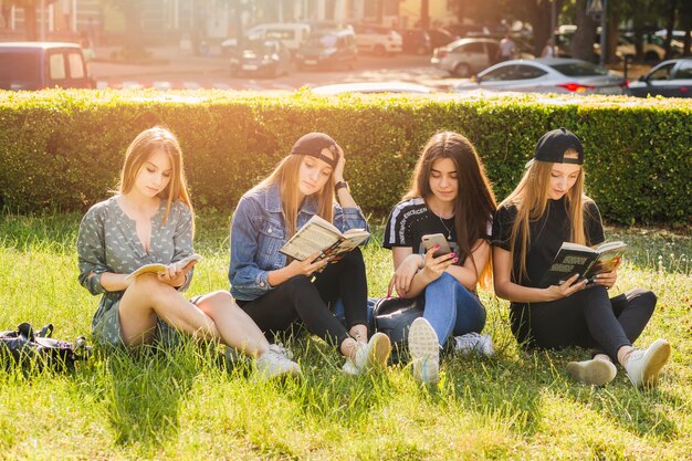 Девочки-подростки, читающие книги и использующие смартфон