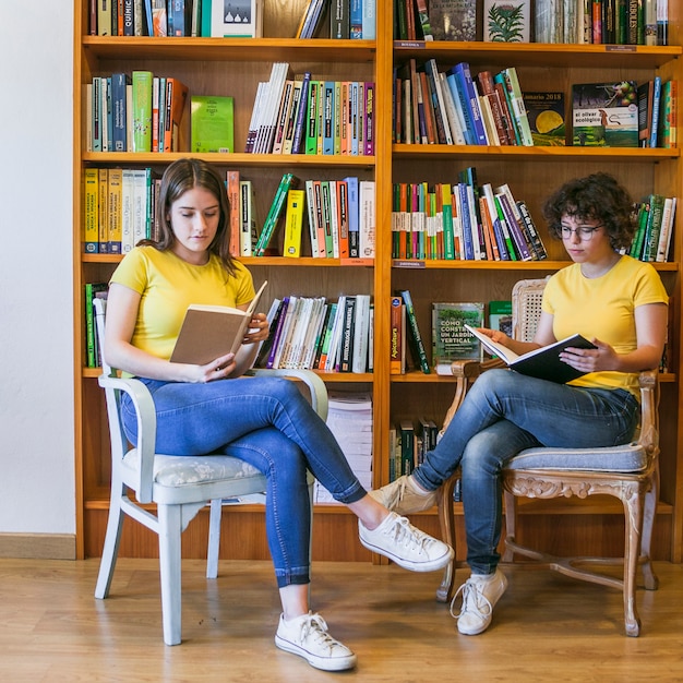 Teen girls reading on chairs near bookcase