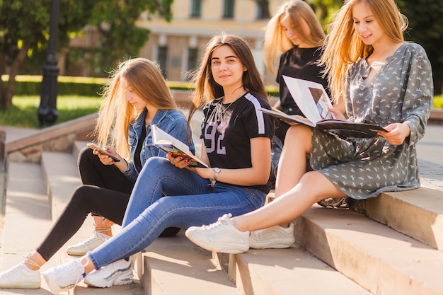 Девочки-подростки с книгой, сидящей среди друзей