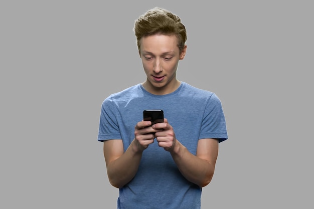 Парень-подросток с помощью смартфона. красивый мальчик-подросток текстовых сообщений на мобильном телефоне сером фоне. молодежь и современные технологии.