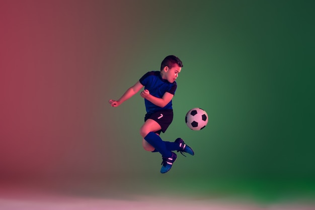 Teen male football or soccer player, boy on gradient background in neon light - motion, action, activity concept